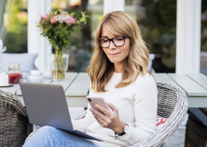 Middle age woman working on phone and laptop on patio