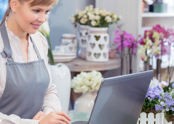 Woman with apron uses laptop at floral shop