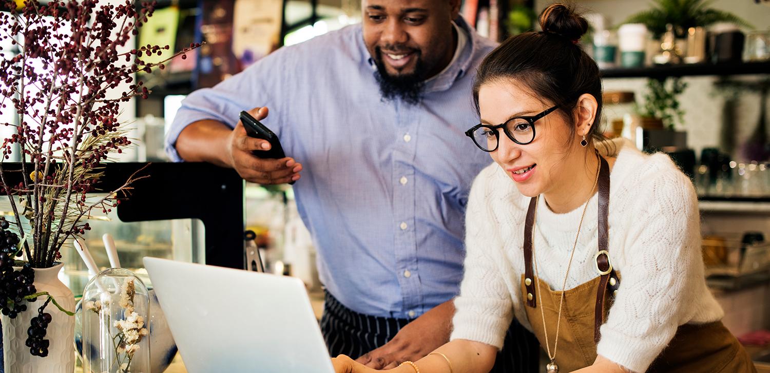 Two small business owners look at a laptop together in a shop.