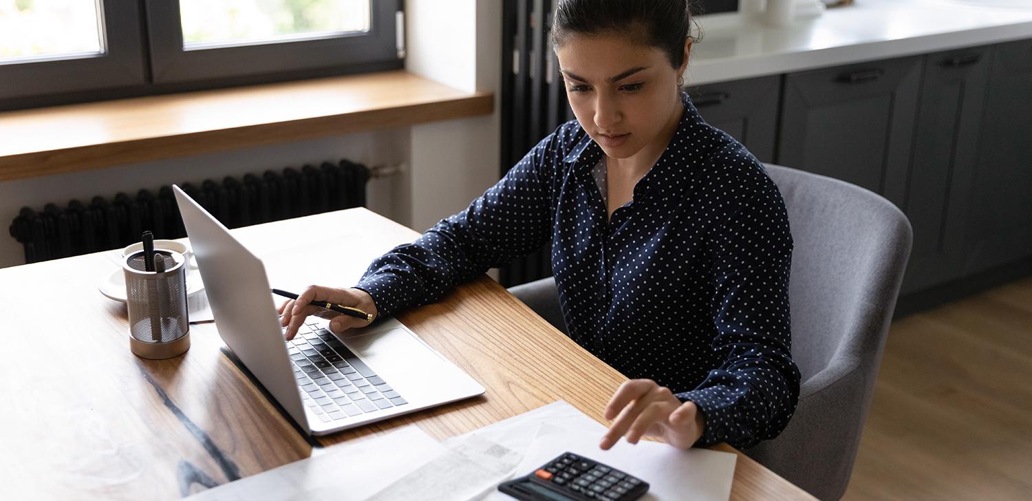 A Small Business Owner Processes Invoices While Looking at a Laptop.