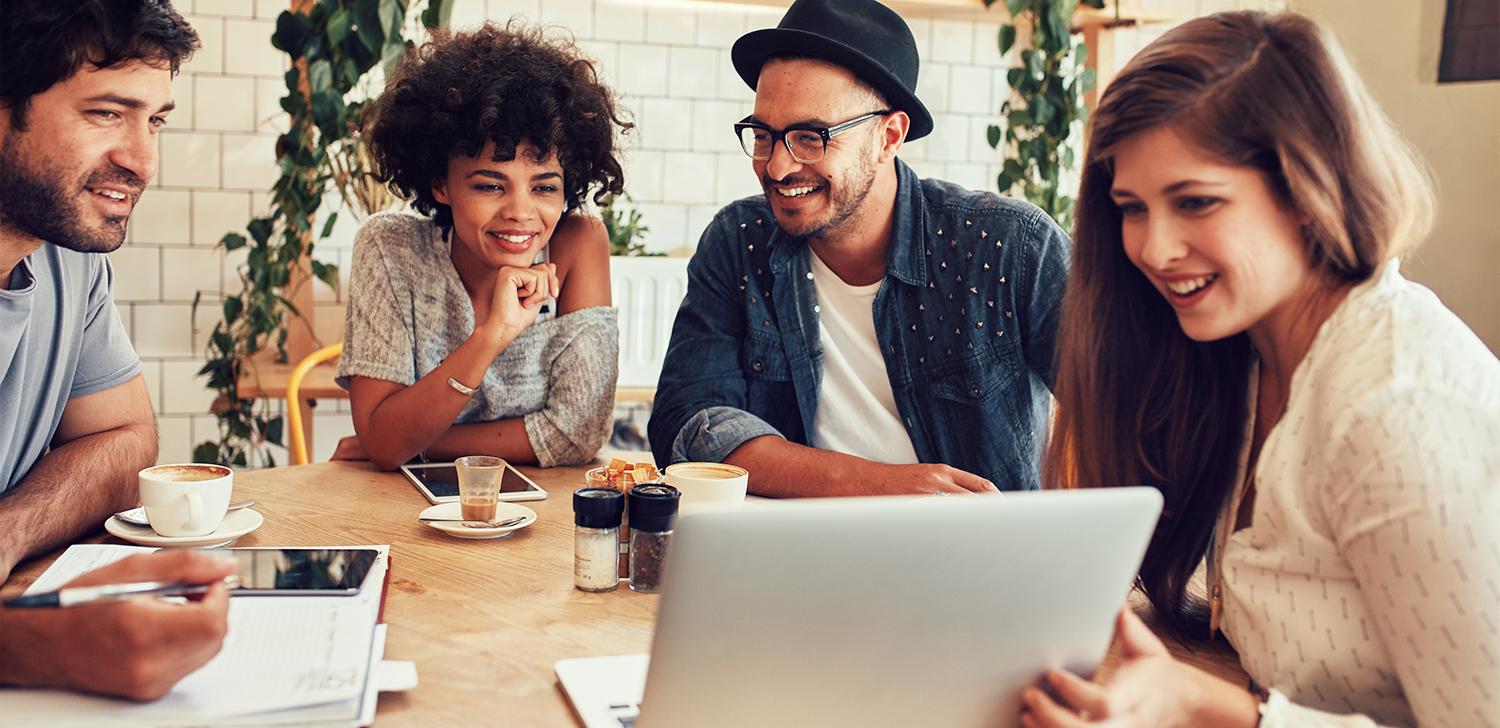 A group of business professionals looking at a laptop screen while sitting around a table.