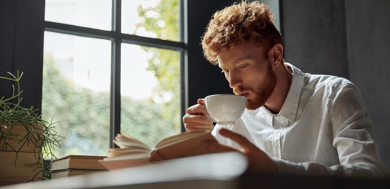 An entrepreneur drinks coffee while reading a book at a table.