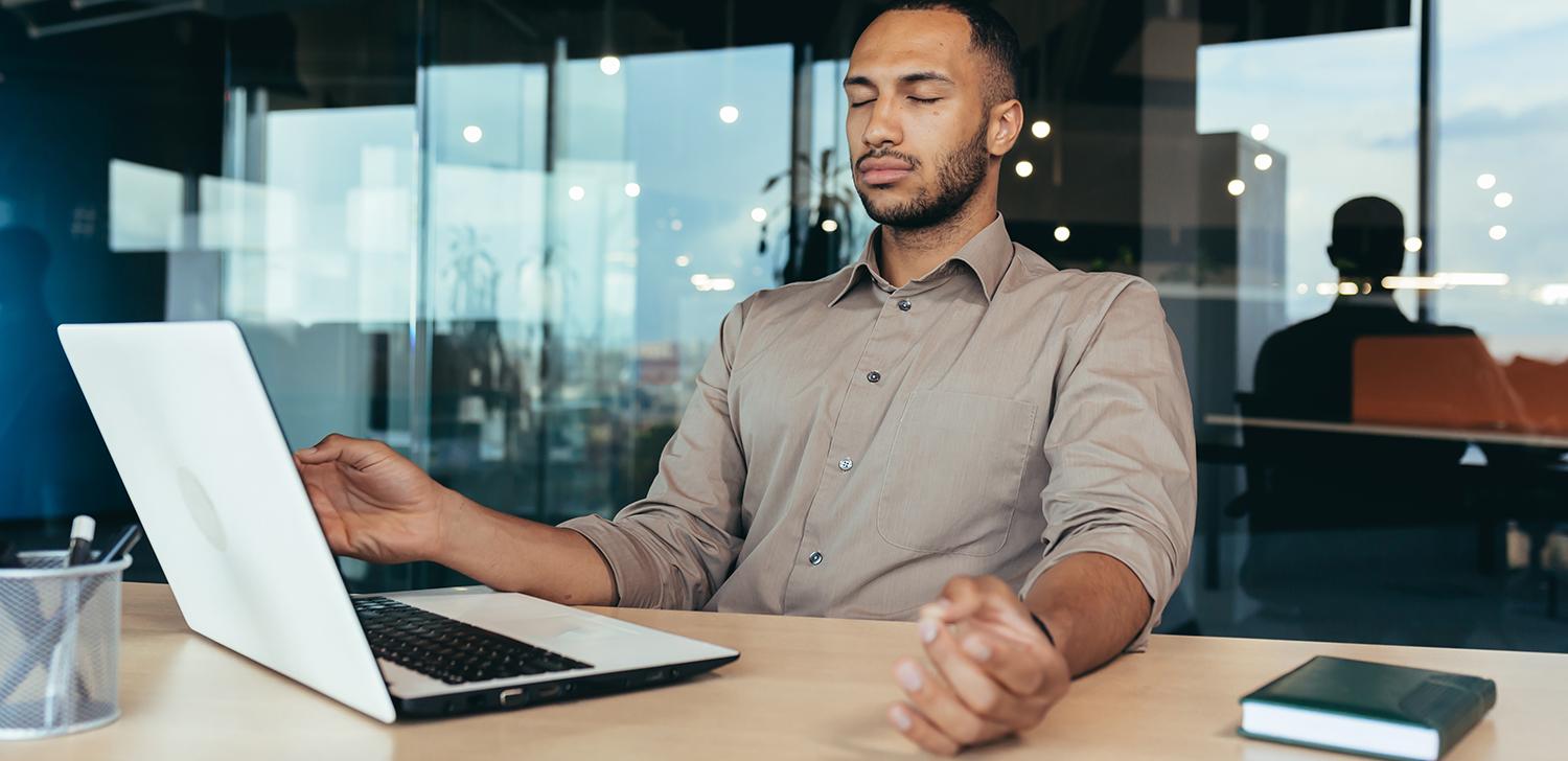 A person with their eye closed sitting at a desk.