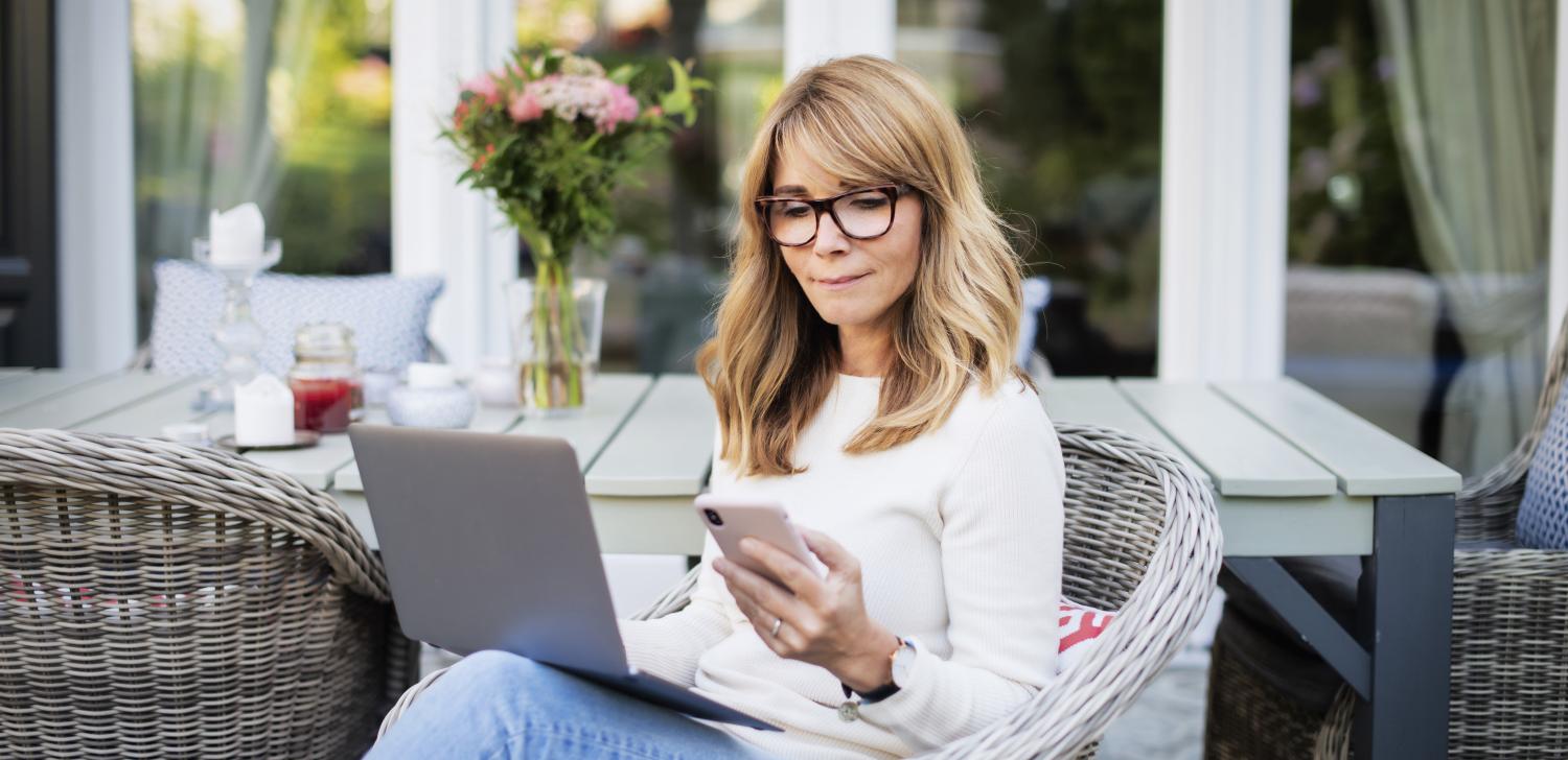 Middle age woman working on phone and laptop on patio